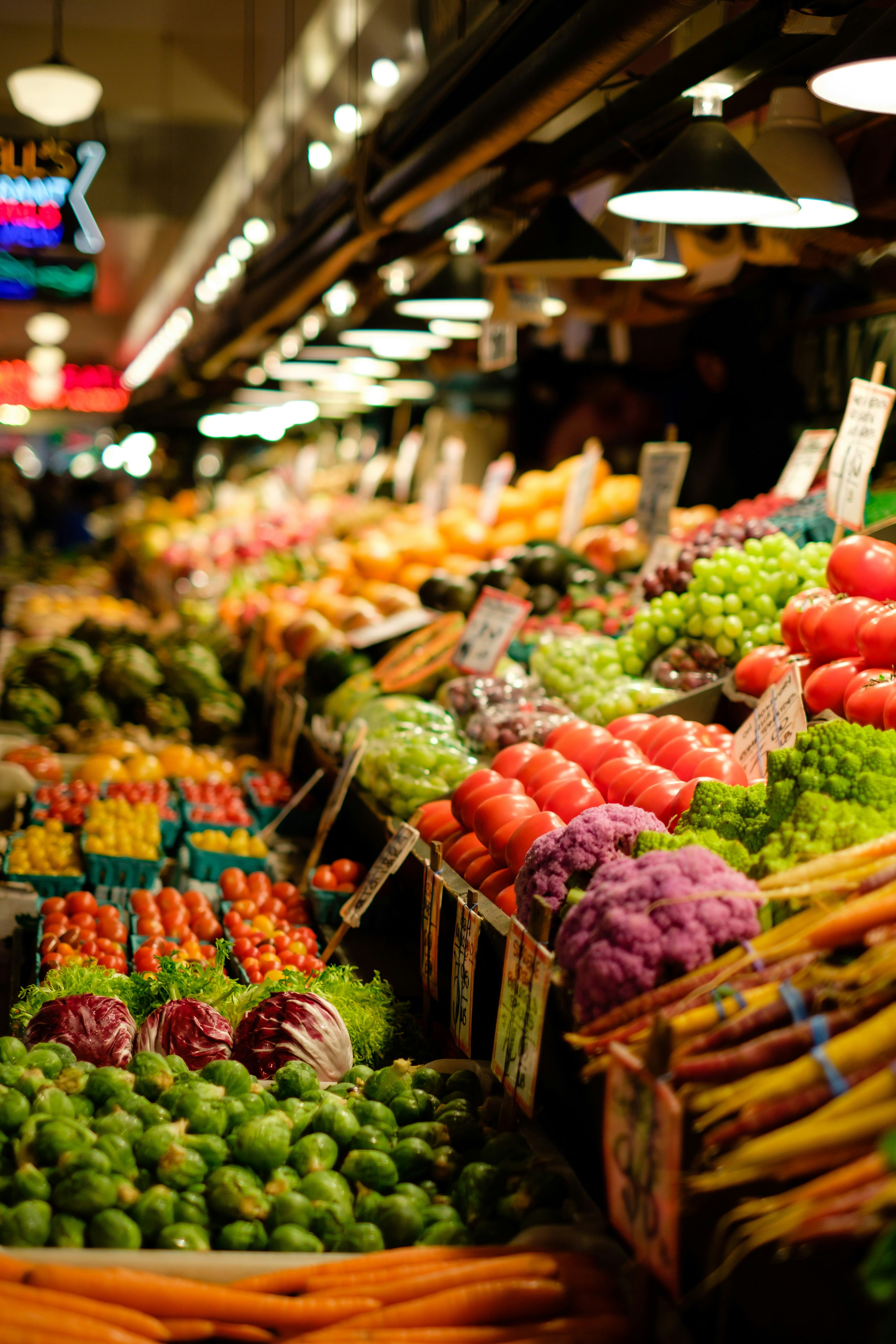 A fresh produce market stall stacked with tomatoes, cauliflower and carrots
